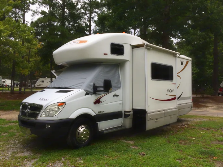 White Winnebago View RV rental parked at a shady campground, ready for adventure. Features an extended slide-out.. Winnebago Avion View 23j 2008