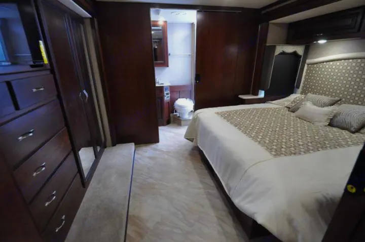 Spacious RV rental interior: bedroom with large bed & dark wood furniture, plus private bathroom access.. Holiday Rambler Vacationer 2017