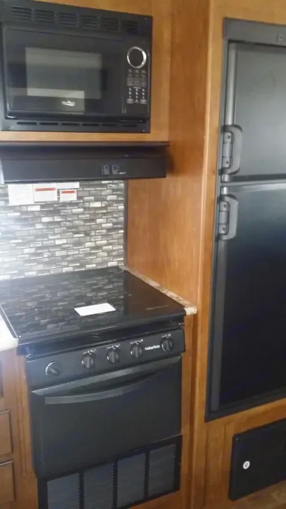 Compact RV rental kitchen: black microwave, Suburban range with oven, and a large refrigerator.. Forest River Salem Cruise Lite 2018