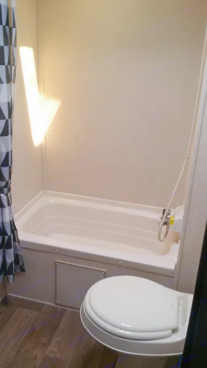 RV rental bathroom with a compact white tub/shower, toilet, wood-look floor, and geometric patterned shower curtain.. Forest River Salem Cruise Lite 2018