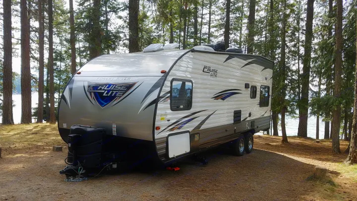 RV rental parked at a serene lakeside campsite, surrounded by tall pine trees. Ideal for a nature getaway.. Forest River Salem Cruise Lite 2017