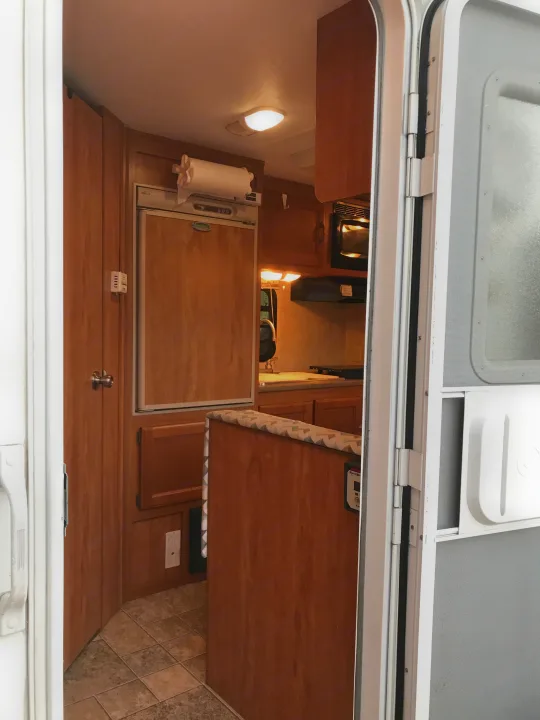 Interior view of an rv rental, featuring a compact kitchen with a microwave, sink, and dinette.. Dutchman Eco 2010
