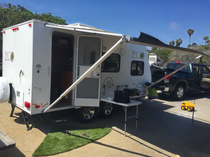 This ECO Skamper rv rental travel trailer is set up at a sunny campsite, complete with an extended awning, grill, and truck.. Dutchman Eco 2010