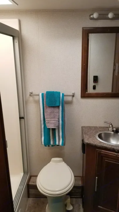 Compact RV rental bathroom featuring a shower, toilet, vanity with sink & mirror, and hanging towels.. Forest River Georgetown 2017