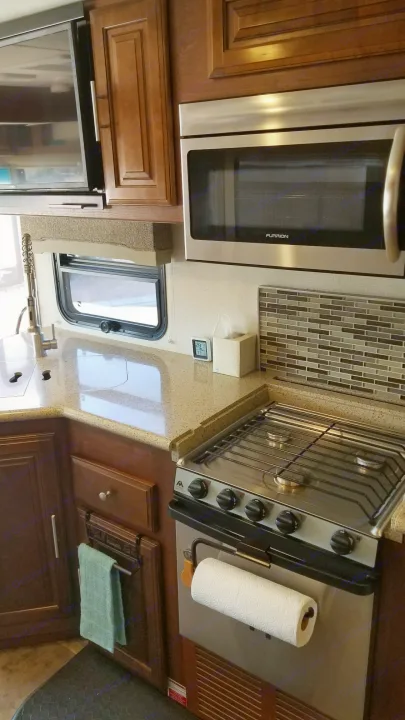 This RV rental kitchen features a stainless microwave, stovetop/oven, sink, and wooden cabinets.. Forest River Georgetown 2017