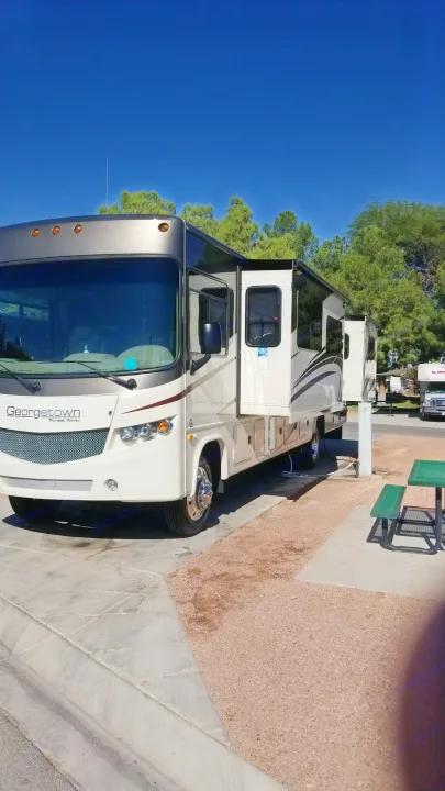 A Georgetown RV rental is parked at a sunny campsite with extended slide-outs and a nearby picnic table.. Forest River Georgetown 2017