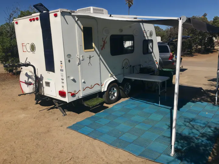 This RV rental campsite shows a white Skamper travel trailer with awning, outdoor table, and blue mat for comfortable living.. Dutchman Eco 2010