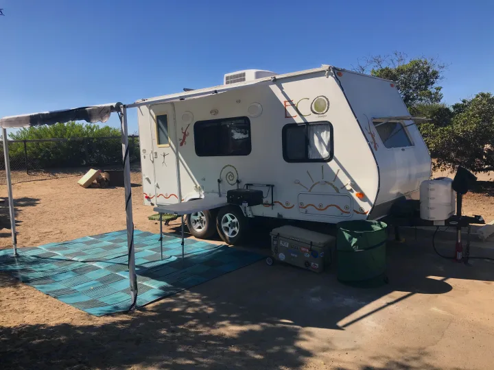 White ECO by Skamper RV rental setup at a sunny desert campsite with an extended awning, blue mat, cooler, and grill.. Dutchman Eco 2010