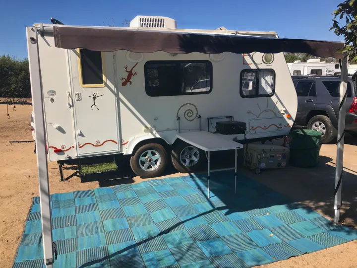This **RV rental** features an extended awning, a blue and green mat, table, and grill, set up for outdoor enjoyment.. Dutchman Eco 2010