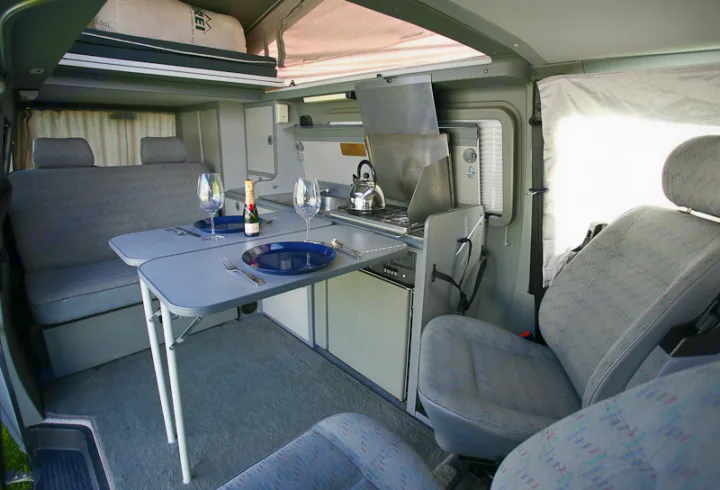 Spacious RV rental interior features a dining area, compact kitchen, and overhead pop-top bed.. Volkswagen Eurovan camper 1999