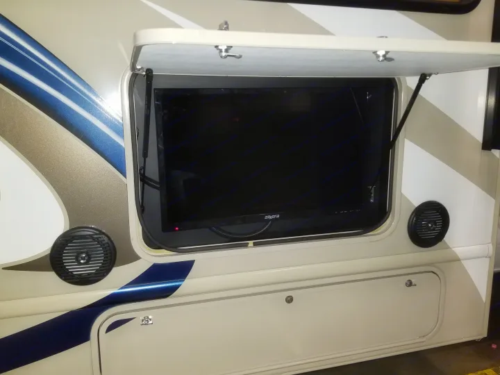 Side of an RV rental showing its outdoor entertainment system: an Axxera TV in a compartment & two external speakers.. Thor Motor Coach Freedom Elite 2018