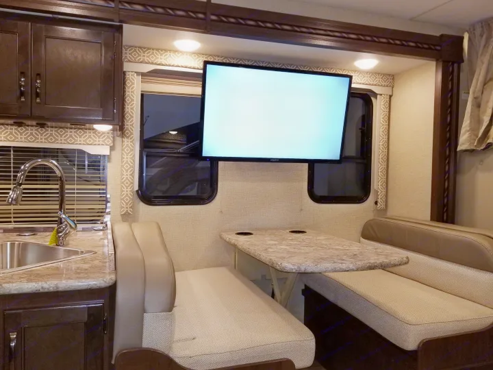 This RV rental interior showcases a compact kitchen, dinette with benches, and a mounted TV, perfect for travel.. Thor Motor Coach Freedom Elite 2018