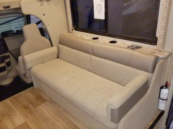 Inside an RV rental: a cozy dinette sofa with integrated cupholders, window views, and durable wood-look flooring.. Thor Motor Coach Freedom Elite 2018