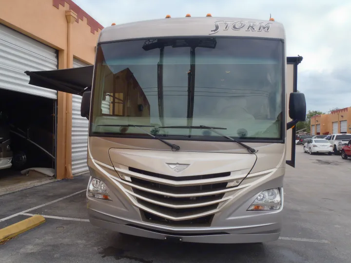 Front view of a beige "STORM" RV, potentially an rv rental unit, parked outside a storage facility.. Fleetwood Storm 2015