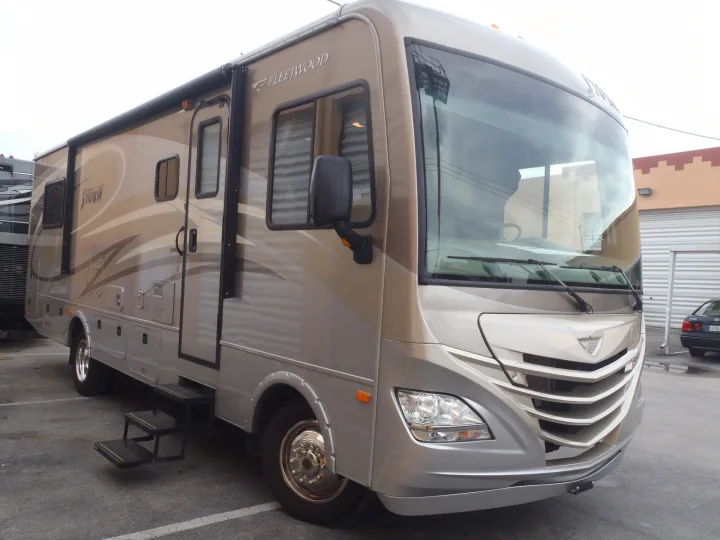 A sleek tan and silver Fleetwood Storm motorhome, perfect for an RV rental. Visible side awning, large windows, and modern front design.. Fleetwood Storm 2015