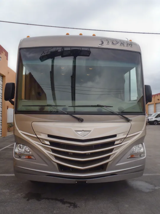Front of a beige 'Storm' RV, ideal for rv rental. Its large windshield reflects buildings & lights. Parked on asphalt.. Fleetwood Storm 2015