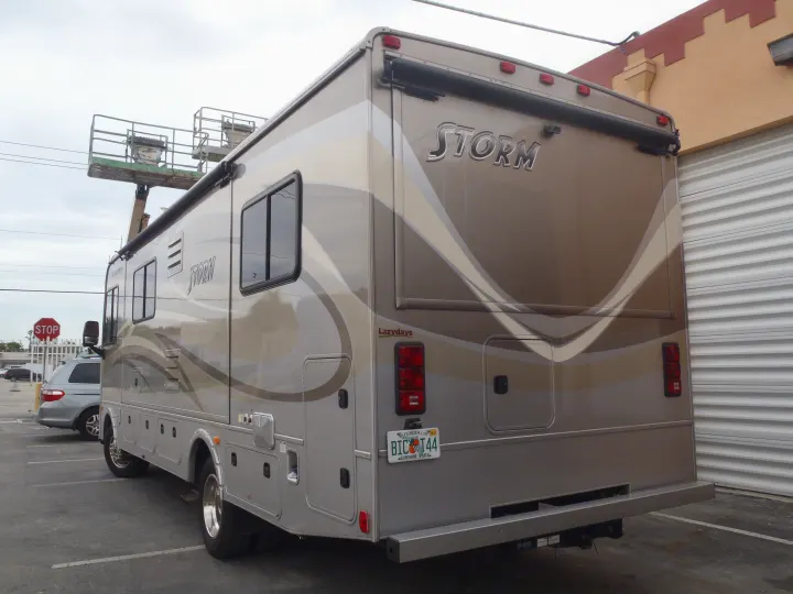 A large, tan Lazydays Storm RV motorhome, likely an RV rental unit, is parked, showing its striped exterior and Florida plate.. Fleetwood Storm 2015