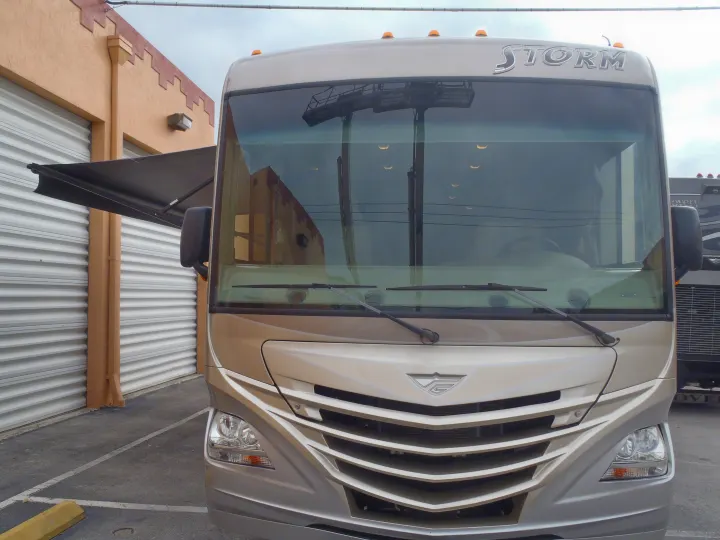 Front of a tan Storm RV with an awning extended, parked by a building. Consider this recreational vehicle for your rv rental.. Fleetwood Storm 2015
