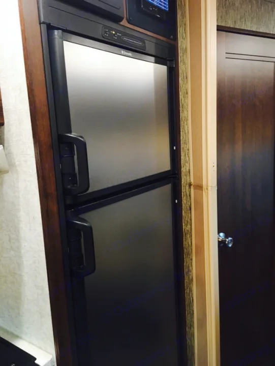 RV rental interior: A compact Dometic refrigerator with two sections, adjacent to a dark wooden door with an ornate knob.. Mercedes Benz Forest River Forester 2017