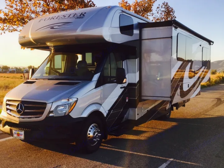A silver and grey Forester Class C RV rental, built on a Mercedes-Benz Sprinter chassis, parked with its side slide-out extended.. Mercedes Benz Forest River Forester 2017