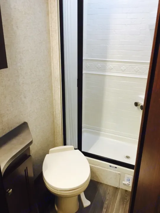 RV rental bathroom features a clean white toilet, built-in shower stall, and stylish wood-look flooring.. Mercedes Benz Forest River Forester 2017