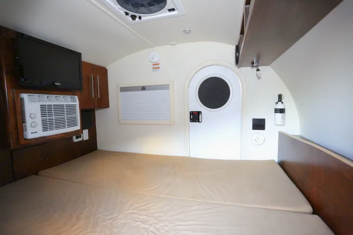 RV rental interior with a cozy bed, TV, AC, window, and a distinctive round door.. T@G MAX 2017