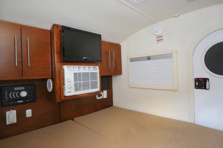 Inside an RV rental, a cozy bed, wood cabinets, TV, AC unit, and control panel provide comfortable amenities.. T@G MAX 2017