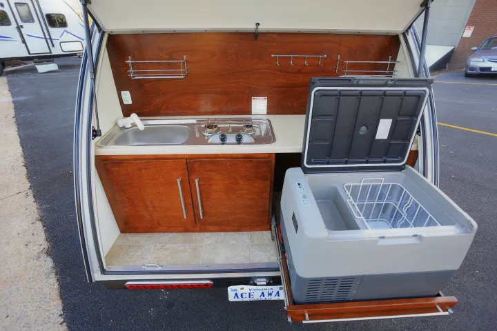 A convenient rv rental outdoor kitchen featuring a sink, two-burner stove, cabinetry, and a pull-out refrigerator.. T@G MAX 2017
