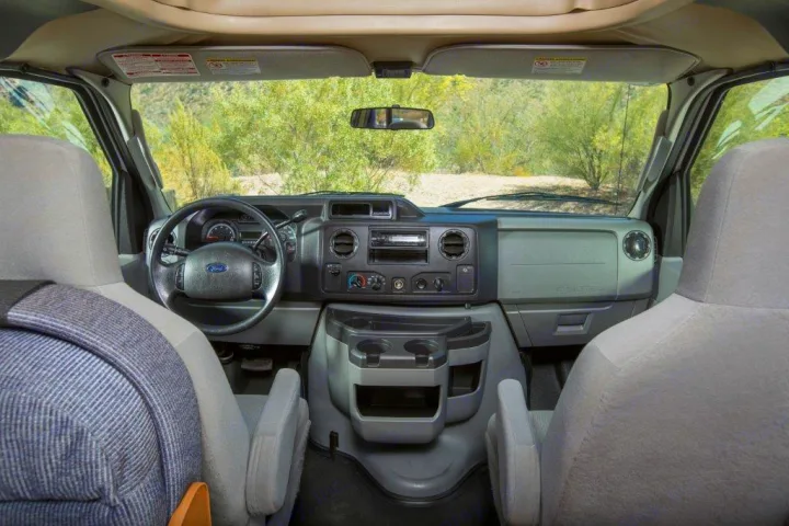RV rental van's interior: Ford dashboard, steering wheel, and front seats, looking out to a scenic road.. Thor 2012 Thor 19G 2012