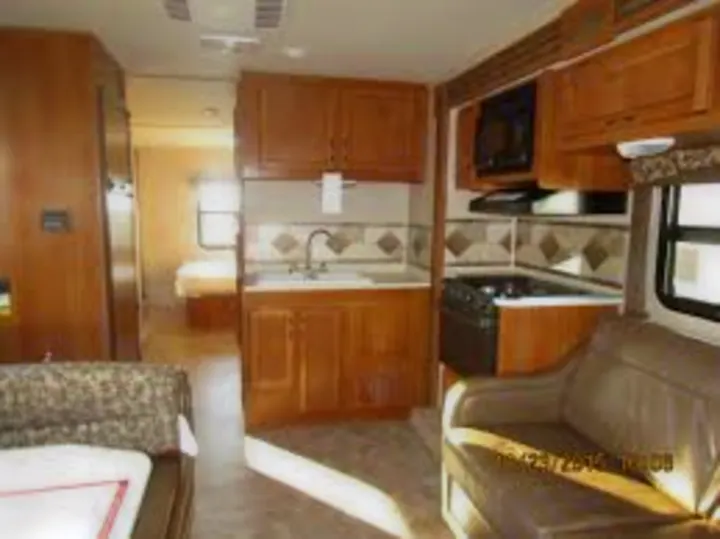 Bright RV rental interior showing a kitchen, living area with sofa, and a bedroom beyond. Ideal for comfortable travel.. Jayco Redhawk 2016