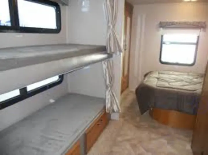 Inside an RV rental, a cozy sleeping area with bunk beds (bottom with storage) and a main bed, ideal for family adventures.. Jayco Redhawk 2016