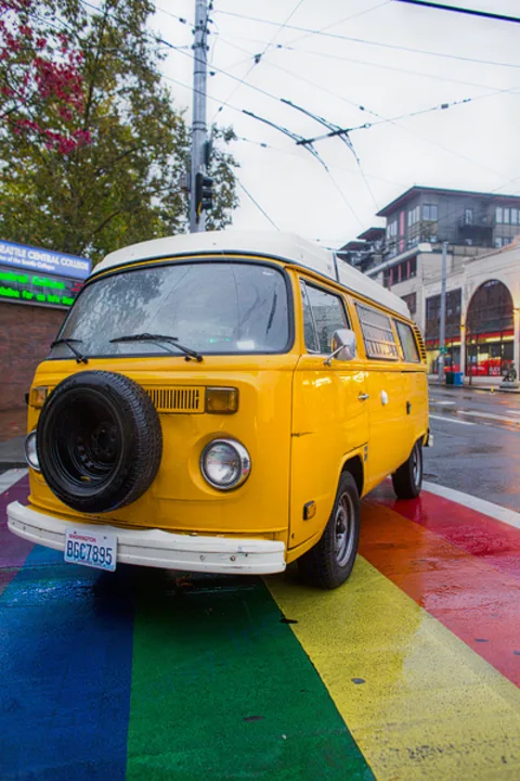 Bright yellow vintage VW camper van with front-mounted spare tire, parked on a wet rainbow crosswalk. Ideal for an RV rental.. Volkswagen Westfalia 1977