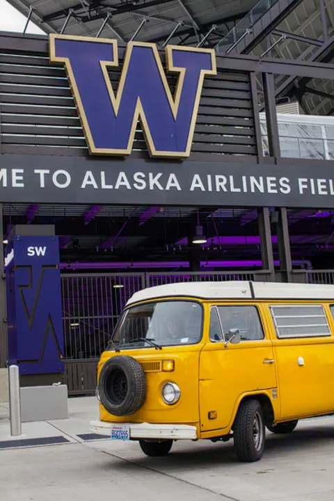 Yellow VW campervan RV rental parked at Alaska Airlines Field's entrance, marked by a huge purple 'W' sign for the Huskies.. Volkswagen Westfalia 1977