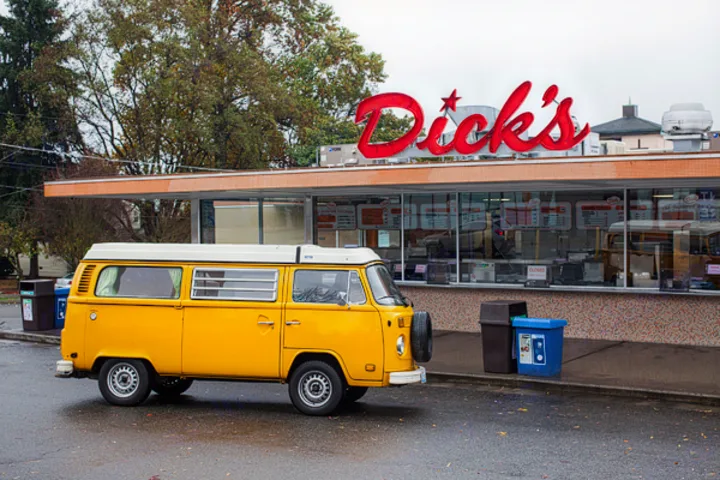A bright yellow vintage VW camper van, perfect for an RV rental, sits outside a Dick's drive-in restaurant on a wet day.. Volkswagen Westfalia 1977