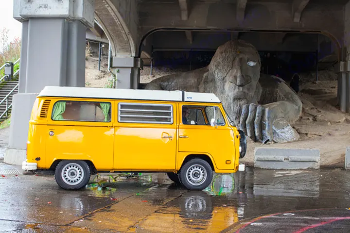 A yellow VW camper van, ideal for an rv rental, parked by Seattle's iconic Fremont Troll under a bridge.. Volkswagen Westfalia 1977