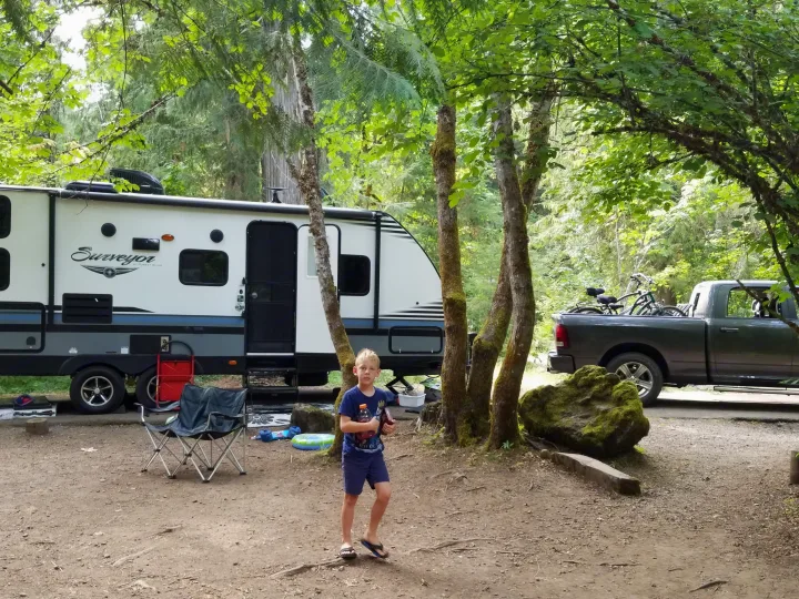 Family camping in a Surveyor travel trailer rv rental at a wooded campsite with a young boy and pickup truck.. Forest River Surveyor 2018