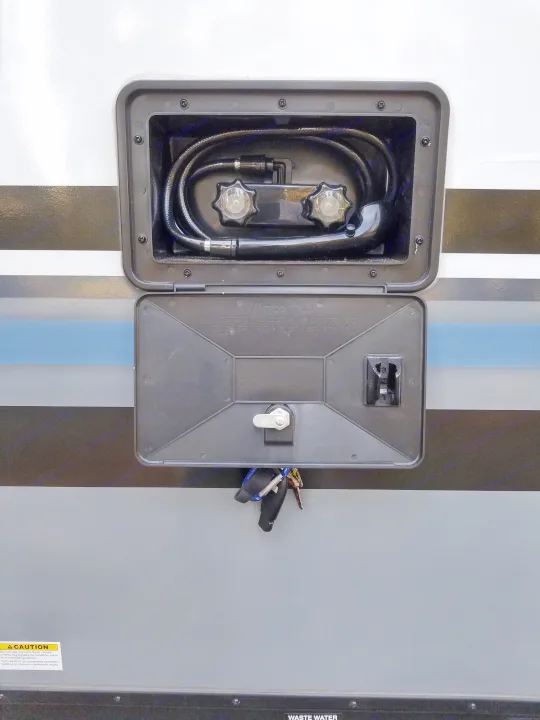 RV rental outdoor shower access panel open, revealing hot/cold taps, hose, and winterizing instructions. Keys are below.. Forest River Surveyor 2018