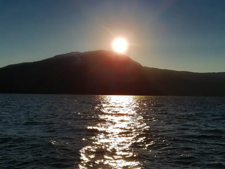 A brilliant sun sets behind a dark mountain, casting golden light on a shimmering lake. Perfect scenery for an RV rental adventure.. Forest River Surveyor 2018