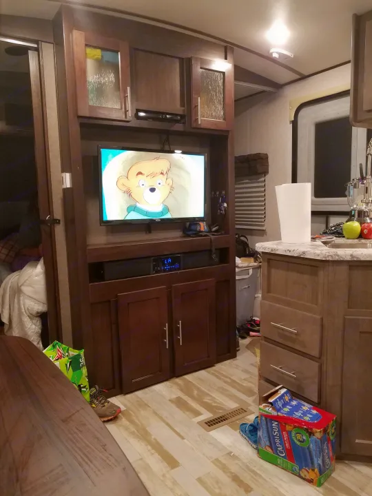 RV rental interior: TV playing cartoons, full kitchen, and sleeping area. A comfy mobile living space.. Forest River Surveyor 2018
