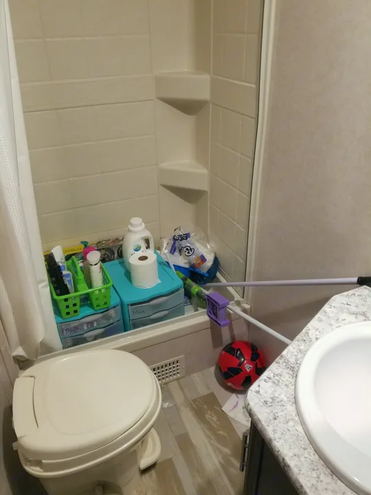 RV rental bathroom showing compact shower, toilet, sink, personal storage, and a red soccer ball on the floor.. Forest River Surveyor 2018