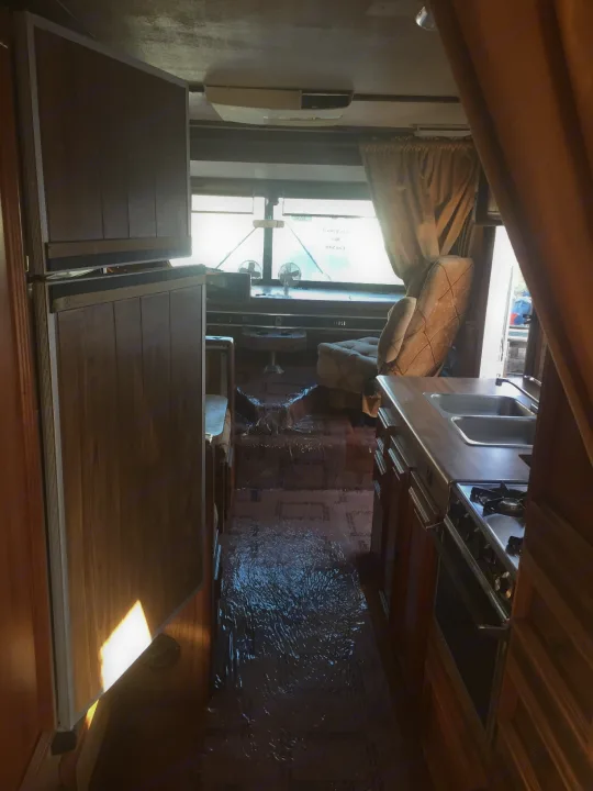 Inside this RV rental: kitchen with sink and stove, living area with windows, and plastic-covered flooring.. Tiffin Motorhomes Allegro 1985