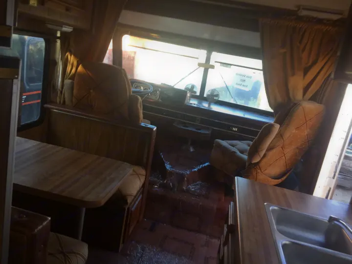 An aged RV interior featuring a cockpit, dining booth, and sink. Debris covers the worn floor, suggesting it's not ready for rv rental.. Tiffin Motorhomes Allegro 1985