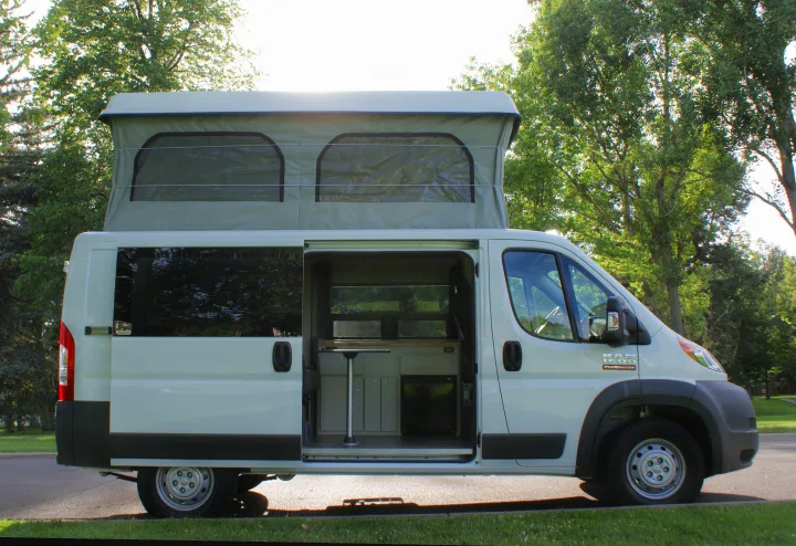A bright white pop-top camper van, great for an RV rental, with its side door open to reveal the cozy interior setup.. Dodge Promaster 2017