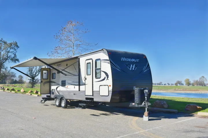 Explore nature! A "Hideout" RV rental parked by a serene lake with its awning extended on a clear day.. Keystone Hideout 2017
