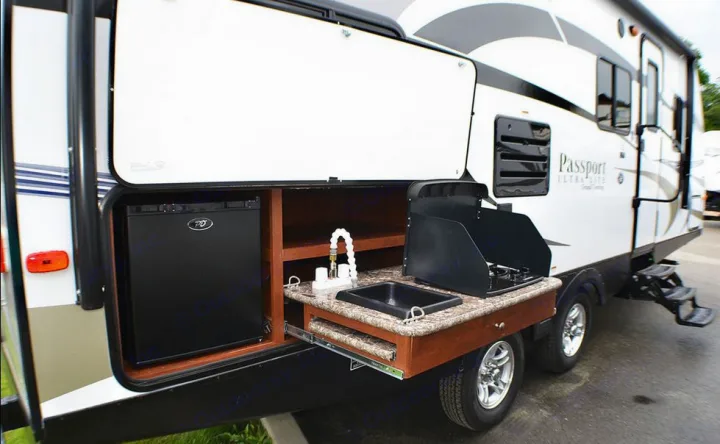 This RV rental travel trailer's side reveals a pull-out outdoor kitchen with a mini-fridge, sink, and stove for camping.. Passport BHS 2015