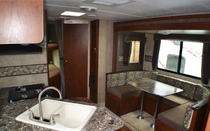 Spacious RV rental interior featuring a kitchen with sink/stove, dining booth, and bunk beds for comfortable travel.. Passport BHS 2015