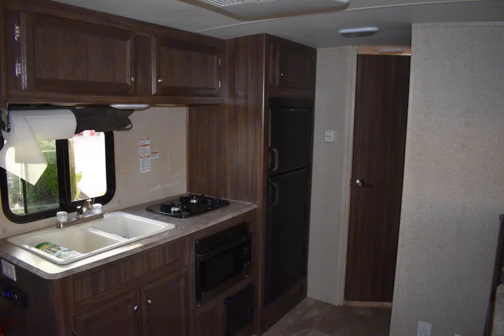 RV rental kitchen showcasing dark wood cabinets, sink, stovetop, microwave, and refrigerator for comfortable travels.. Coachmen Apex 2018