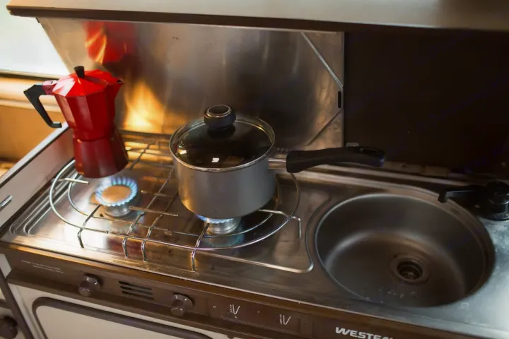 Compact RV rental kitchen featuring a moka pot, saucepan on gas burners, and a sink. Ideal for travel cooking.. Volkswagen Westfalia 1986