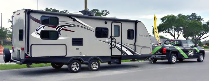 A light grey travel trailer, an rv rental, is shown being towed by a black pickup truck with green Herbalife branding.. Keystone RV Passport Elite 2017