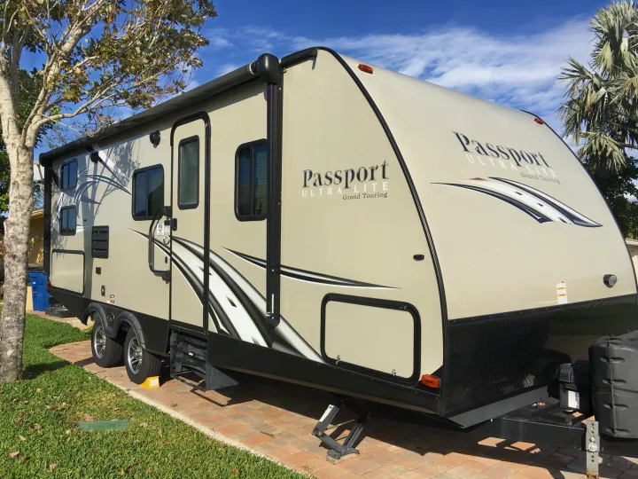 Side view of a light tan Keystone Passport travel trailer (RV), ready for adventure as an rv rental. Parked outdoors.. Keystone RV Passport Elite 2017
